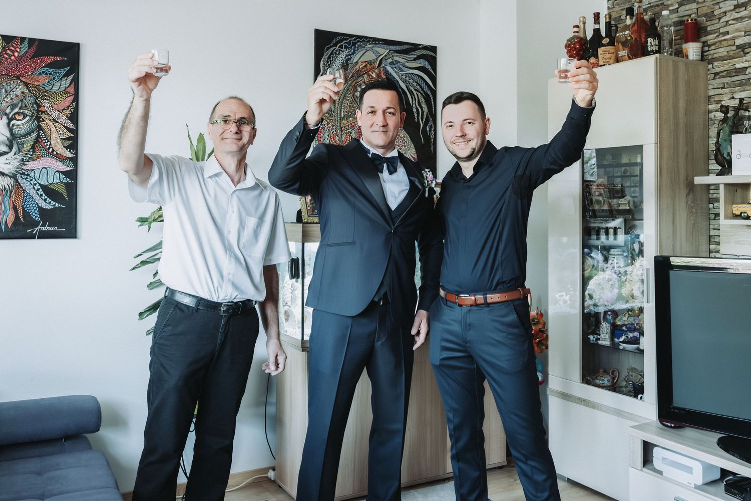 Three excited individuals celebrating with raised drinks in a modern living room interior.