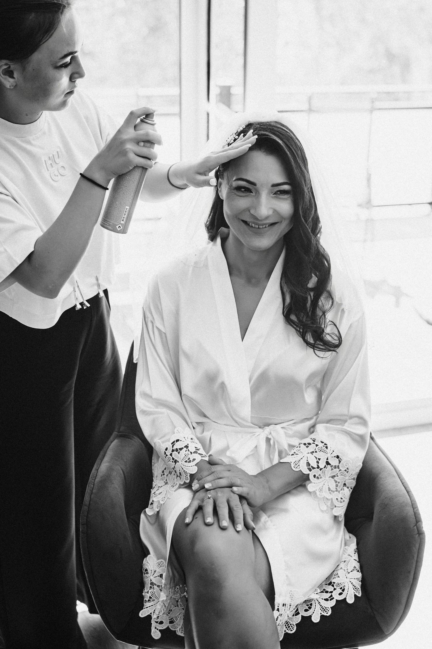 Person having hair styled while seated in white robe with lace trim.