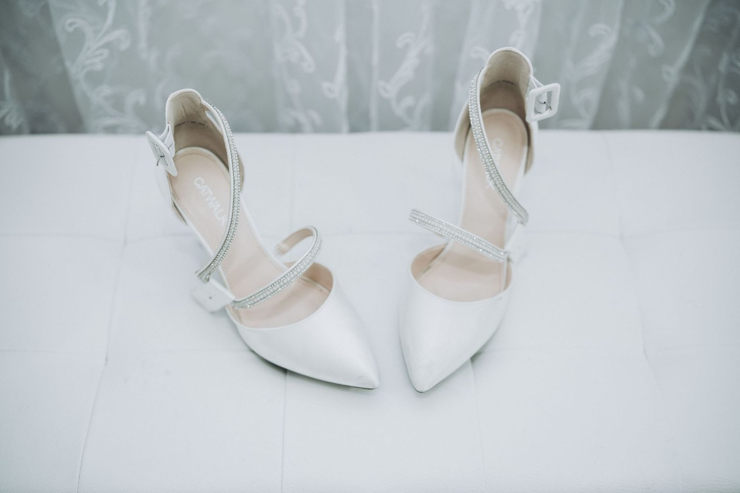Elegant white bridal shoes with straps displayed on white surface.