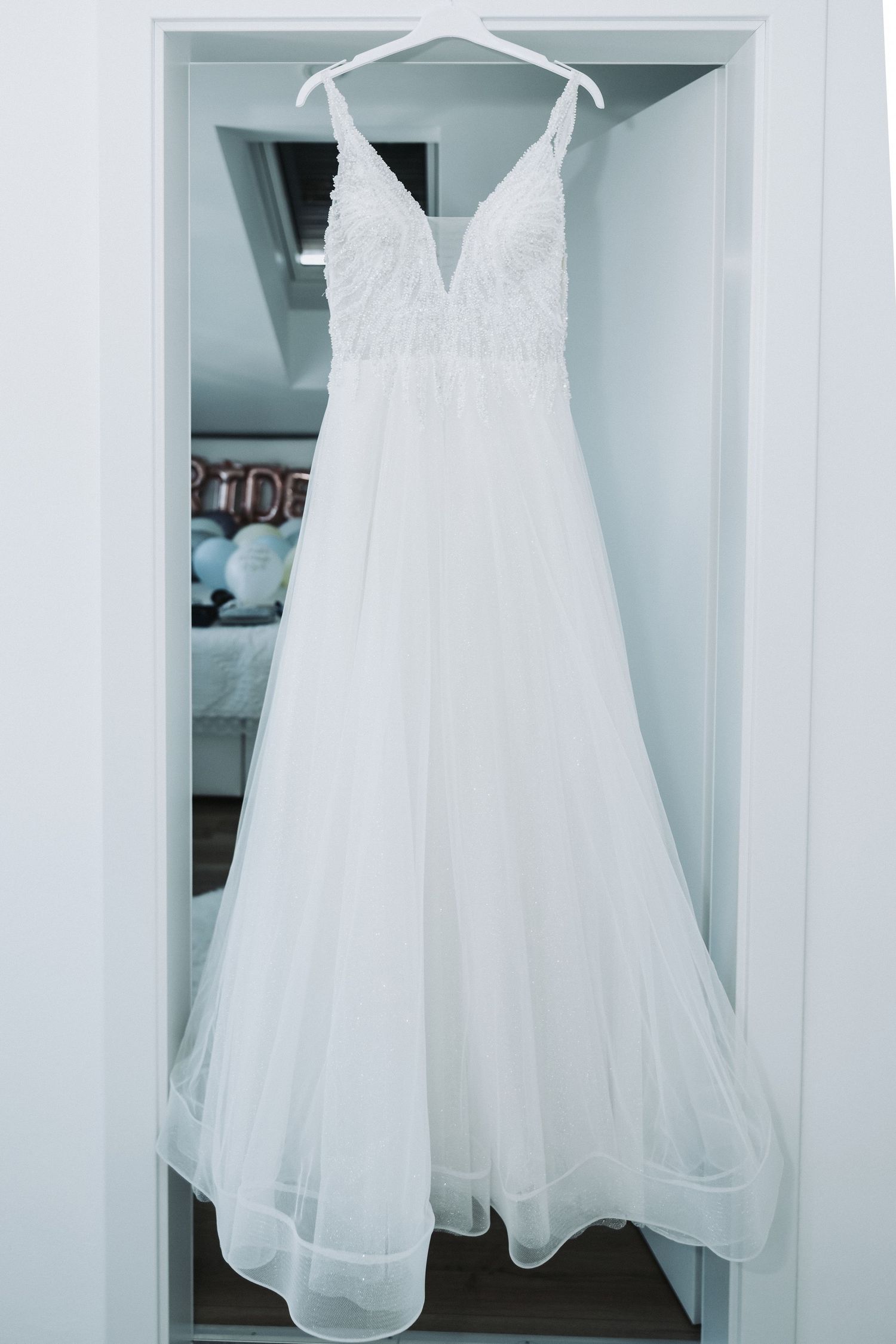 White wedding dress with plunging neckline and flowing tulle skirt hanging in closet.