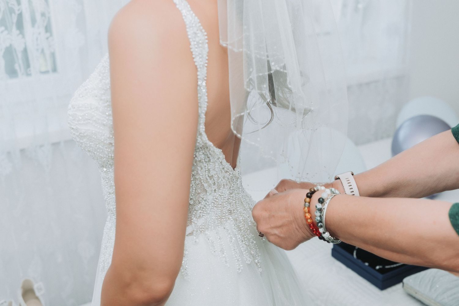 Close-up shot of someone adjusting the back of a white beaded wedding dress with delicate details.