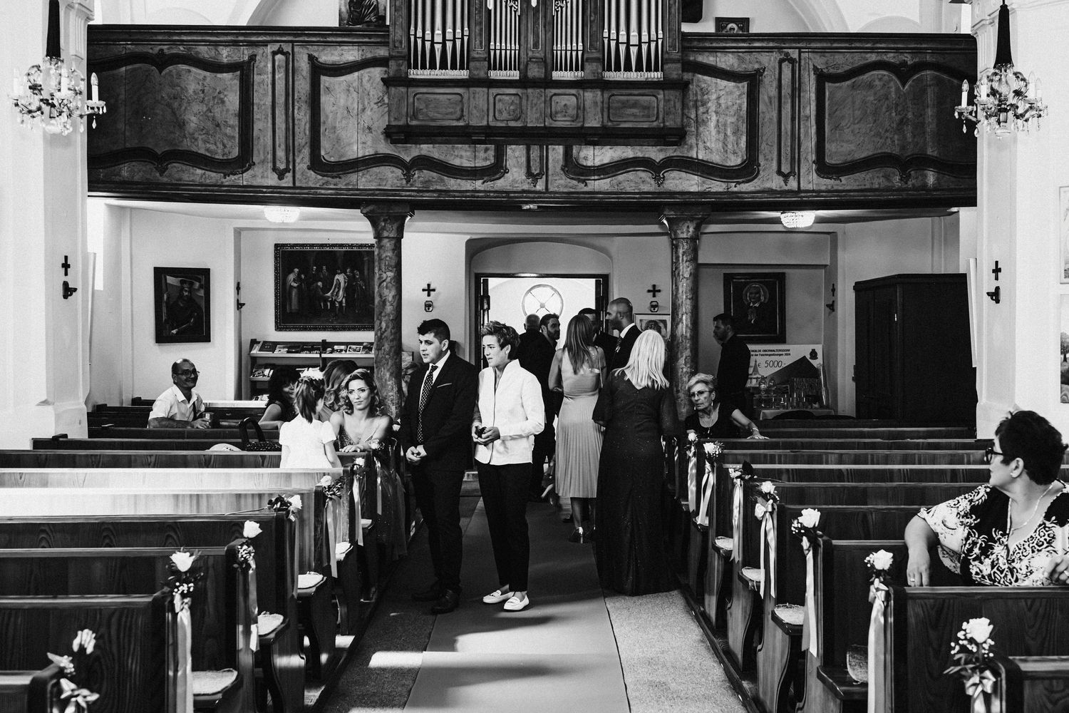 Black and white photo of people gathering inside a traditional church with wooden pews.