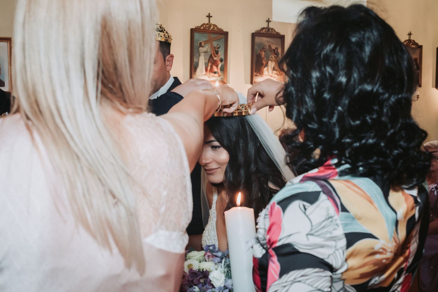 Wedding guests help prepare the bride for her special day in a church with religious artwork on the walls.