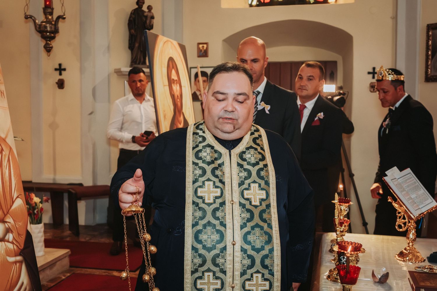 Priest in ornate green vestments conducting religious ceremony in church with traditional decorations.