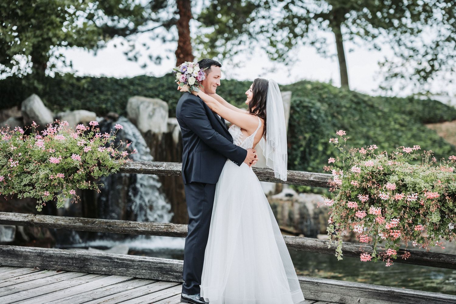 Couple embracing on rustic wooden boardwalk surrounded by pink flowers.