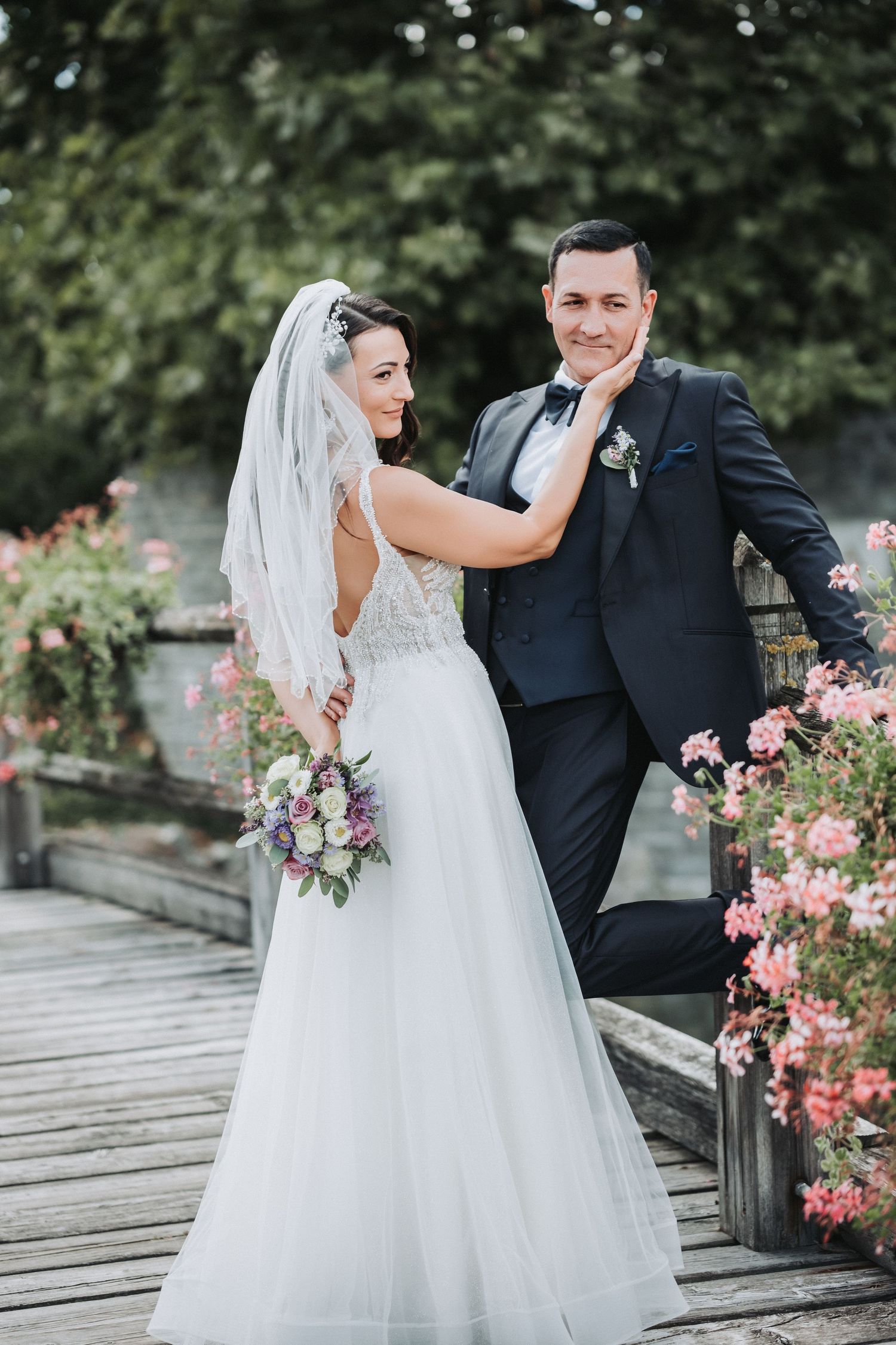 Bride in flowing white dress poses playfully with groom on wooden walkway.