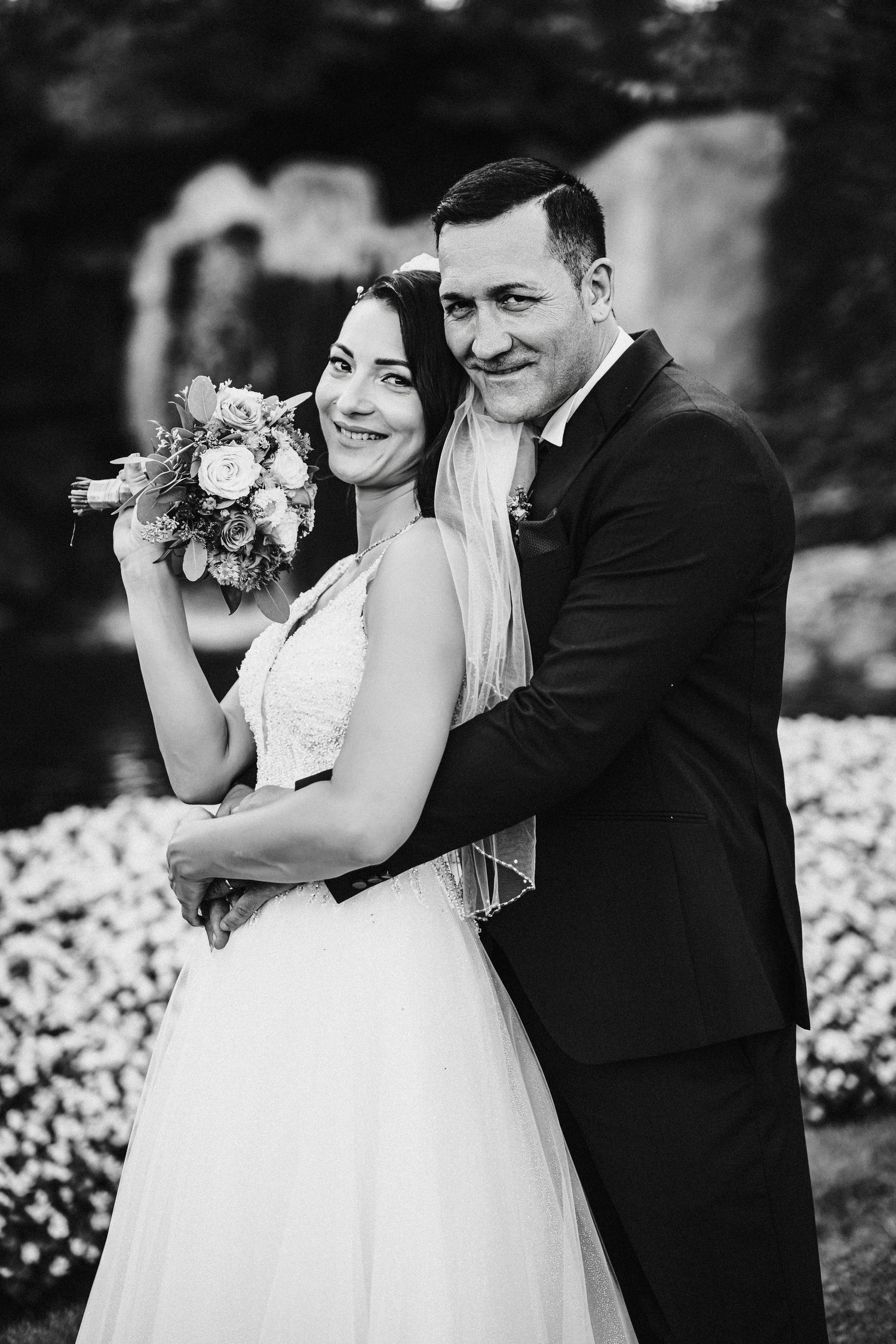 Black and white portrait of a happy couple in wedding attire holding a floral bouquet.