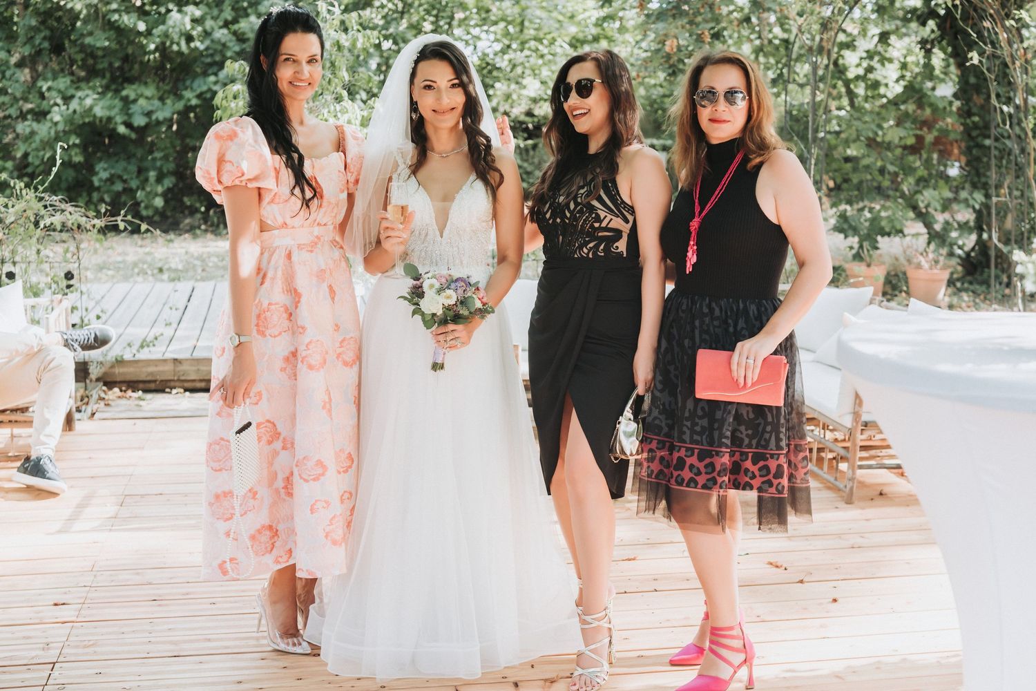 Wedding party in colorful dresses posing together on wooden deck.