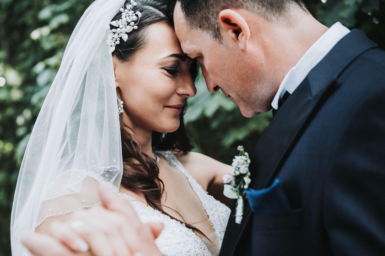 Intimate close-up of newlyweds sharing a tender forehead touch while embracing outdoors.