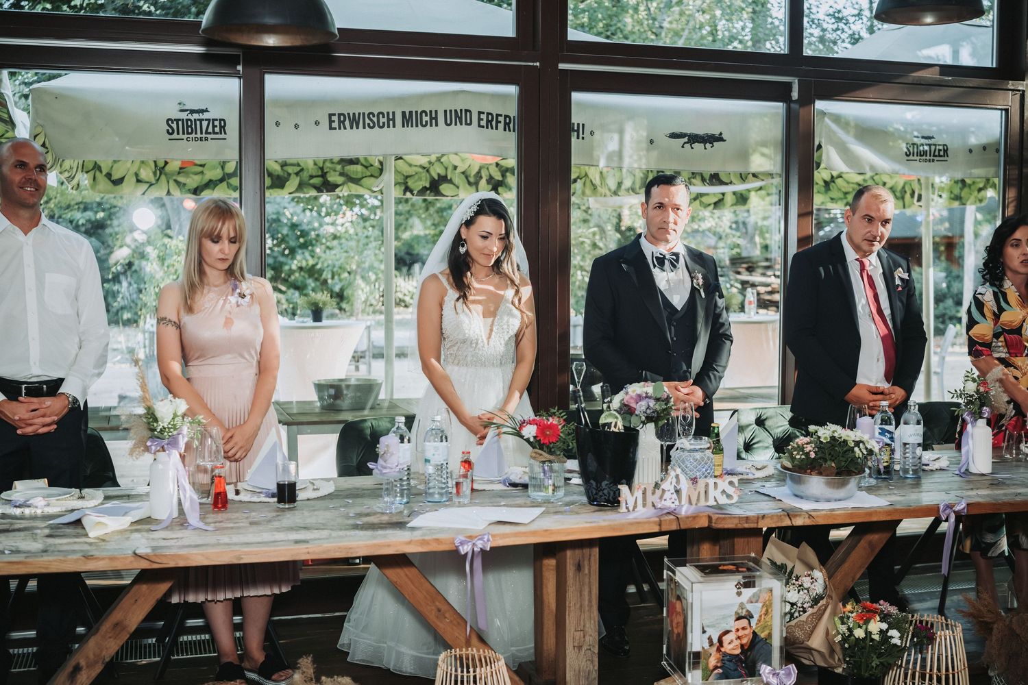Wedding party members stand at a head table during reception toasts.
