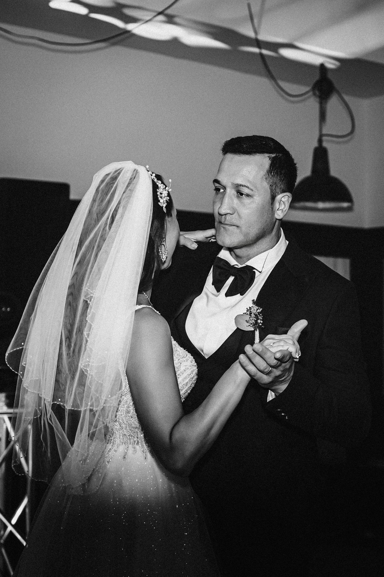 A black and white photo captures a romantic wedding dance moment under pendant lights.