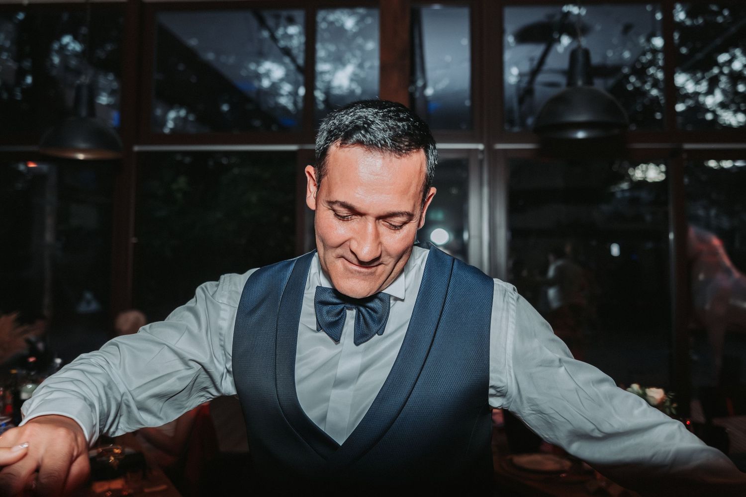 A man in a vest and bowtie smiles while dancing at a wedding reception.