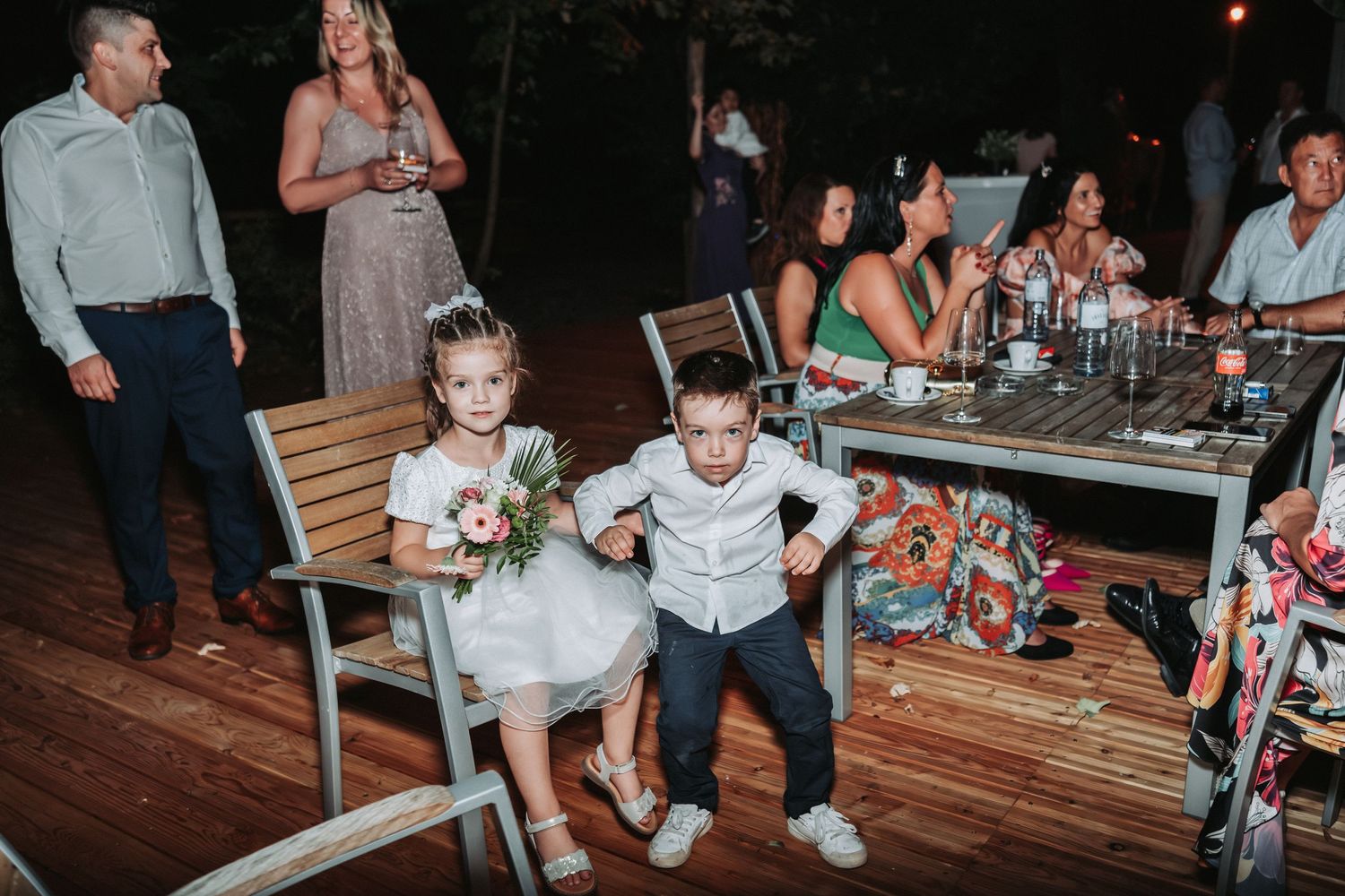 Two young children in formal attire dance together on a wooden deck during a wedding reception.