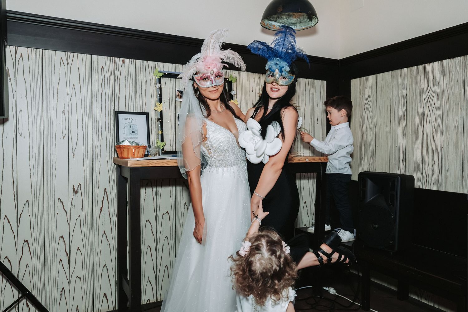 Wedding party members pose for fun photos with props in a room with textured wallpaper.