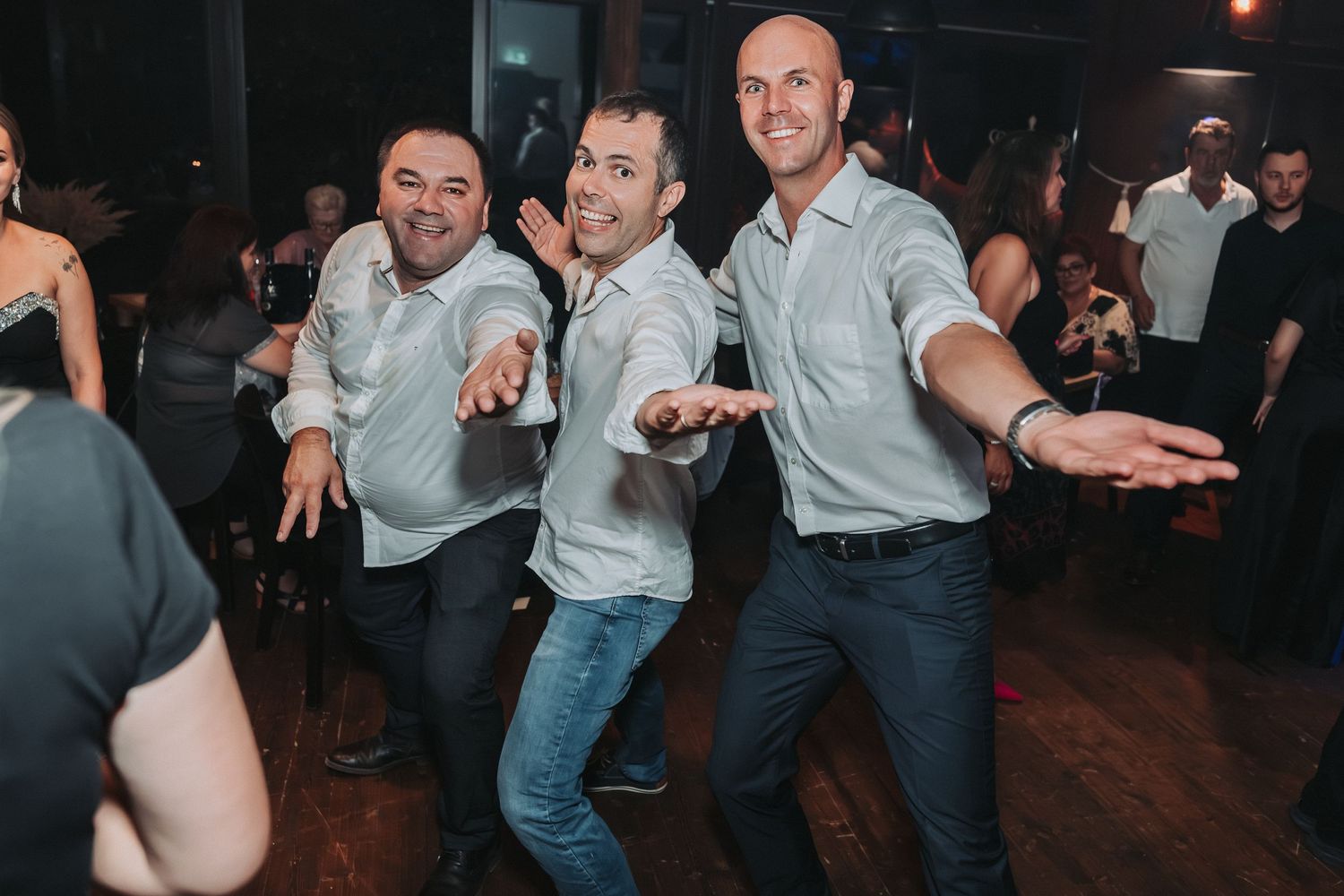 Three groomsmen perform a synchronized dance move at a wedding reception.