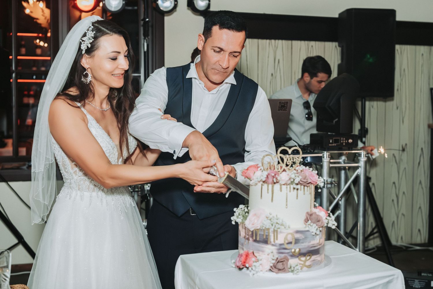 A couple cuts their pink-decorated wedding cake together at the reception.