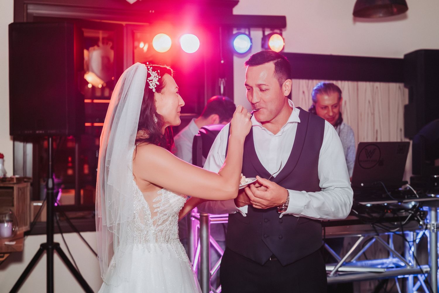 A couple shares an intimate dance moment at their wedding reception under colorful lighting.