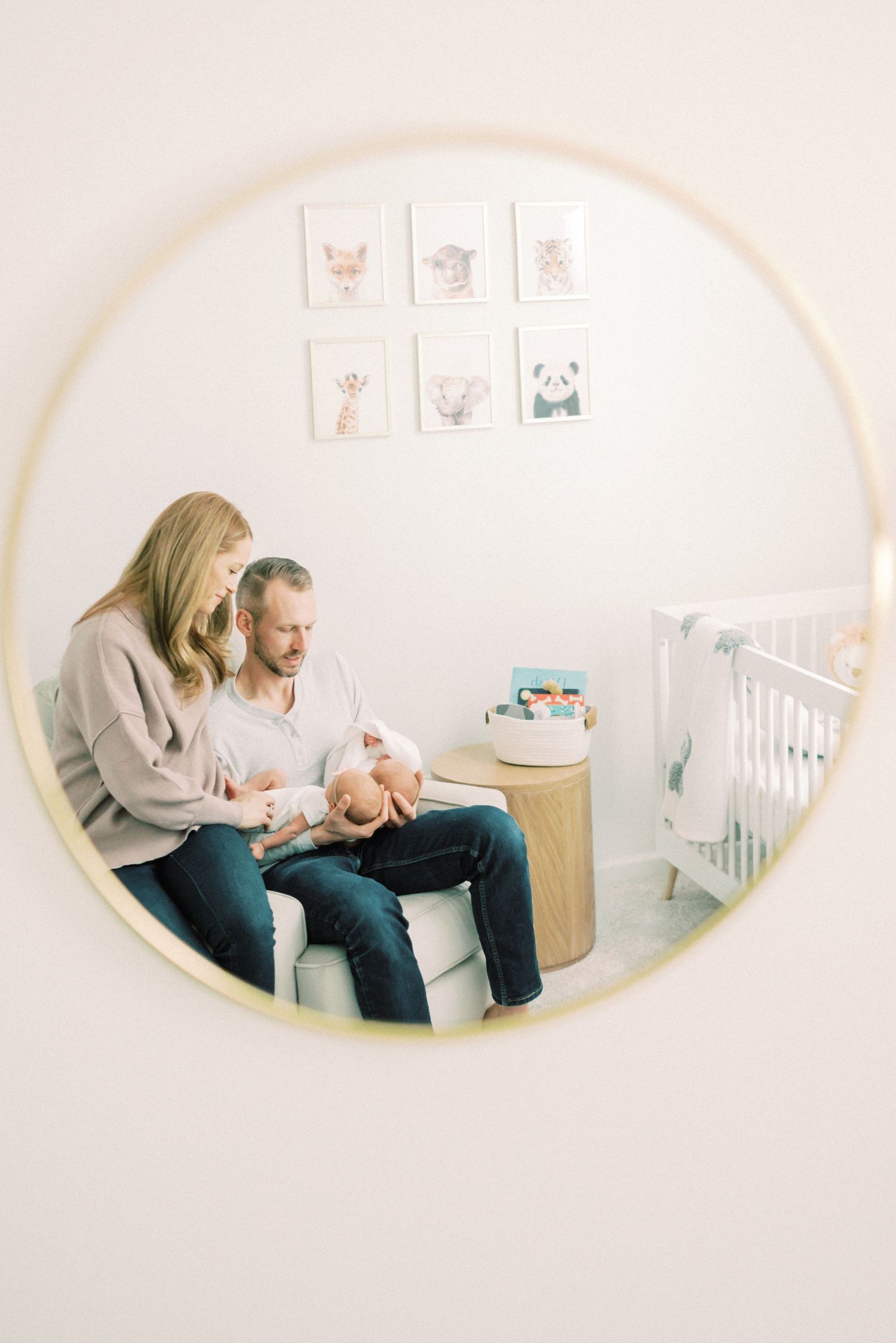 Nursery room reflection in a round mirror showing a family with their newborn and animal artwork on wall.