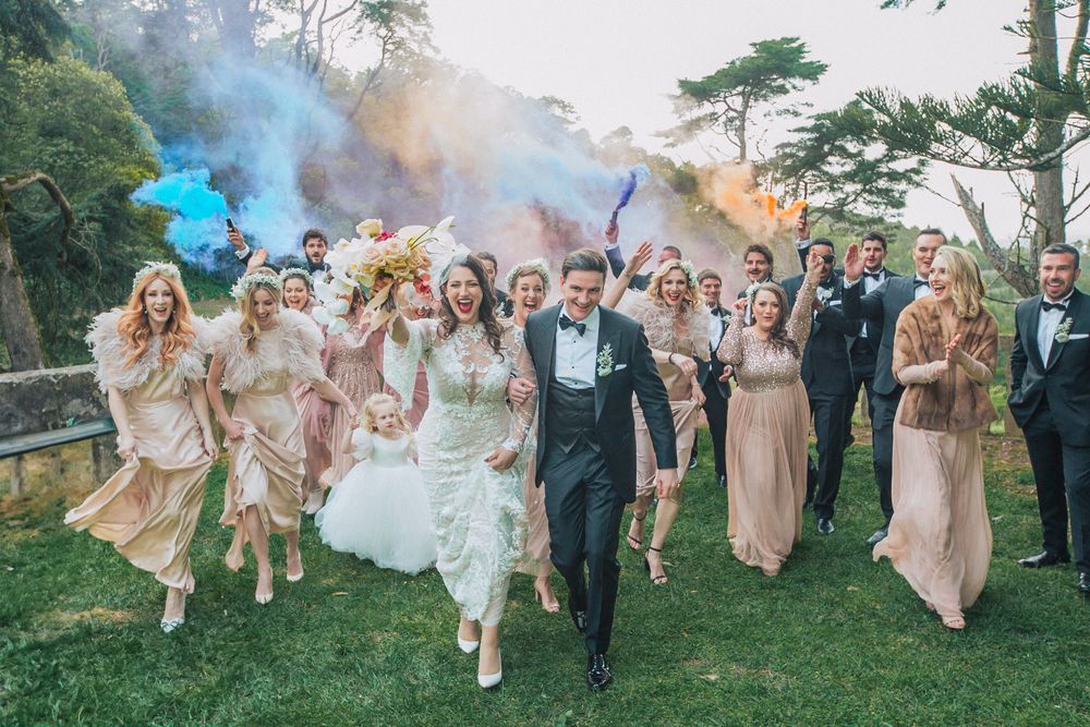 Wedding party running through colorful smoke bombs during outdoor celebration. captured by a Portugal wedding photographer