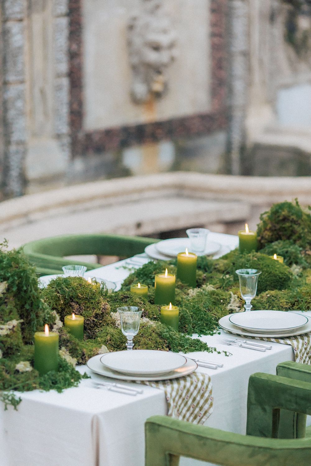 An elegant wedding table setting with green candles and moss decorations against a classical backdrop.