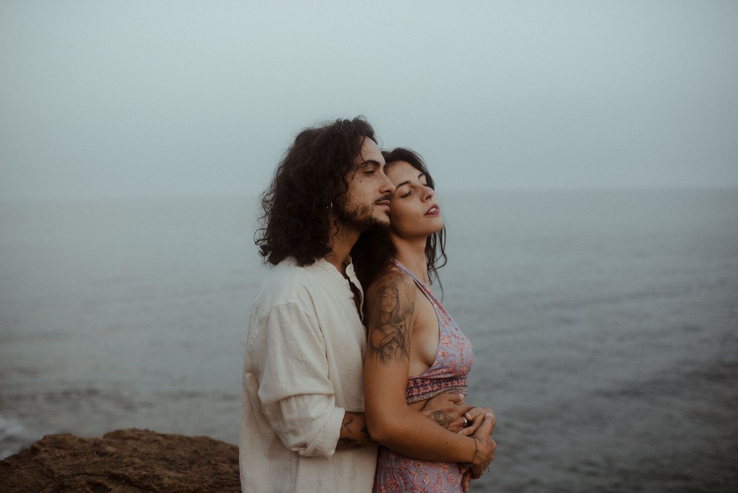 A couple sharing an intimate moment while standing on ocean cliffs at dusk.
