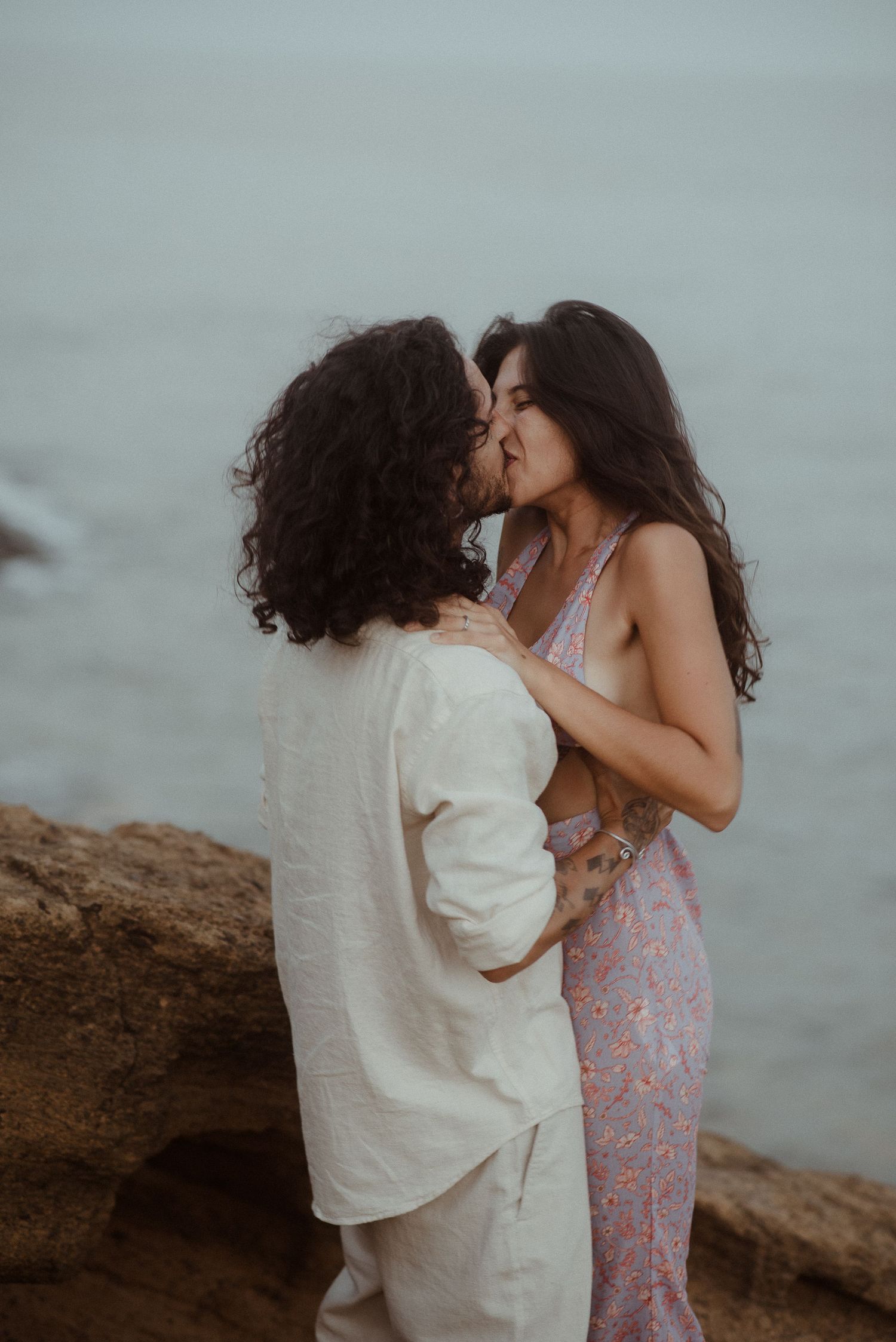 A tender romantic moment between a couple on rocky cliffs overlooking the sea.