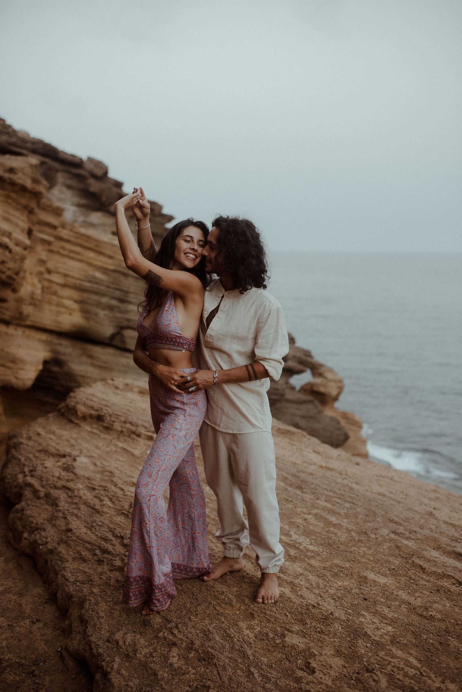 Couple dances together on rocky cliff edge with ocean view.