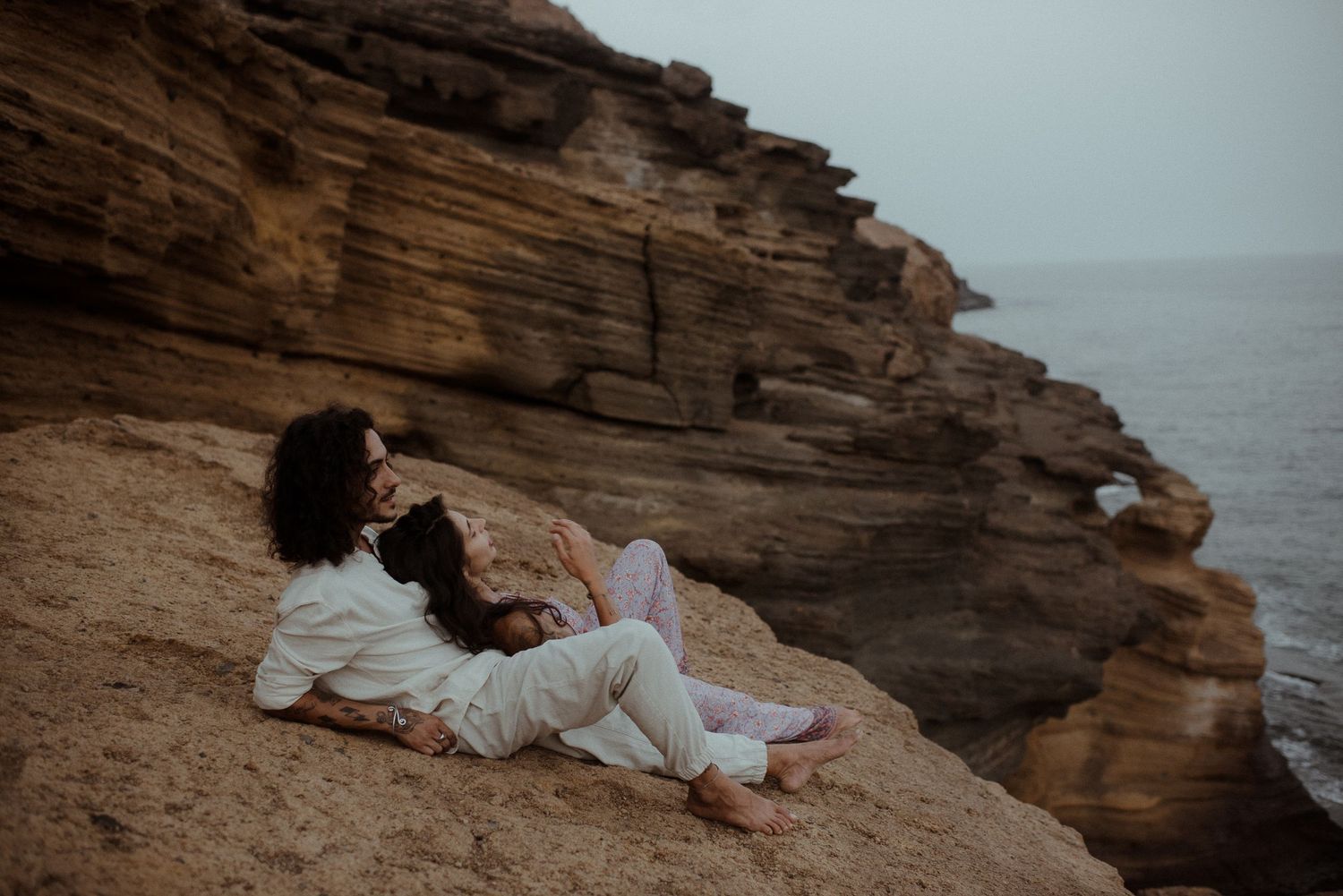 Couple relaxes on rugged coastal cliff overlooking the ocean.