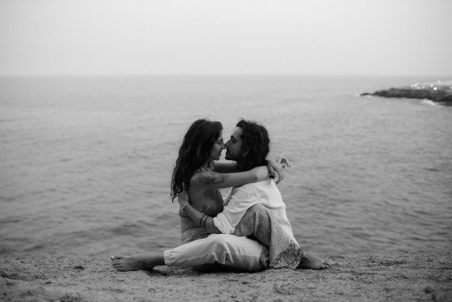 Black and white photo of couple embracing on misty ocean cliff.