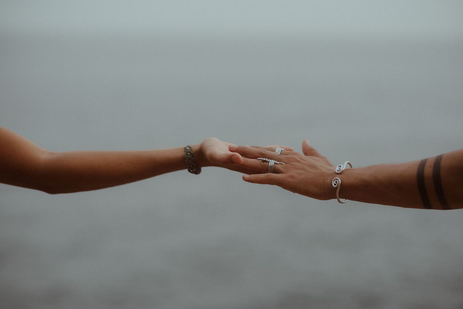 Two hands reach towards each other against a misty gray background in an intimate gesture.