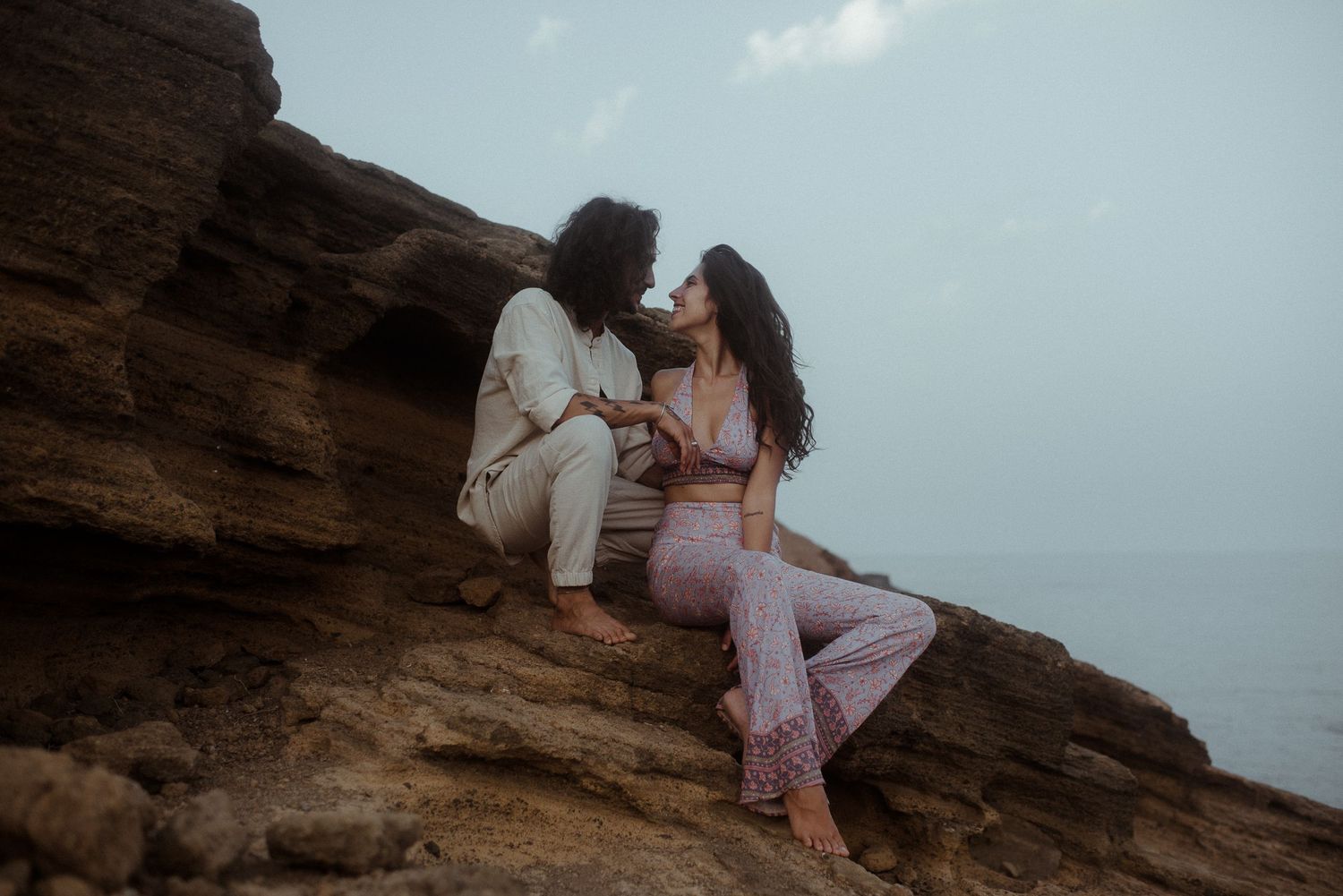 Romantic couple sharing intimate moment on rocky seaside cliff at dusk.