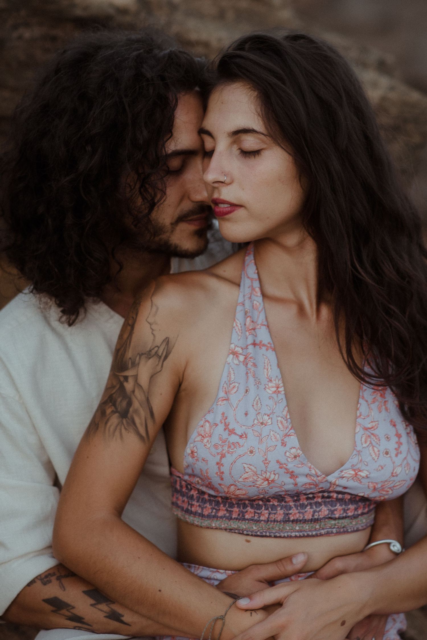 Intimate close-up of couple in casual bohemian outfits against rocky backdrop.
