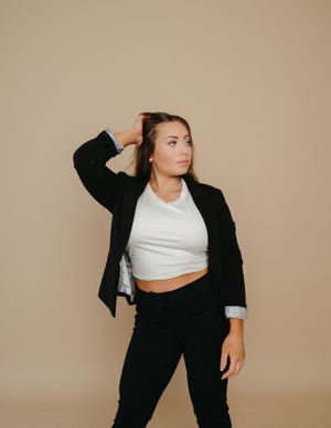 Fashion portrait in black blazer and white crop top against beige background.