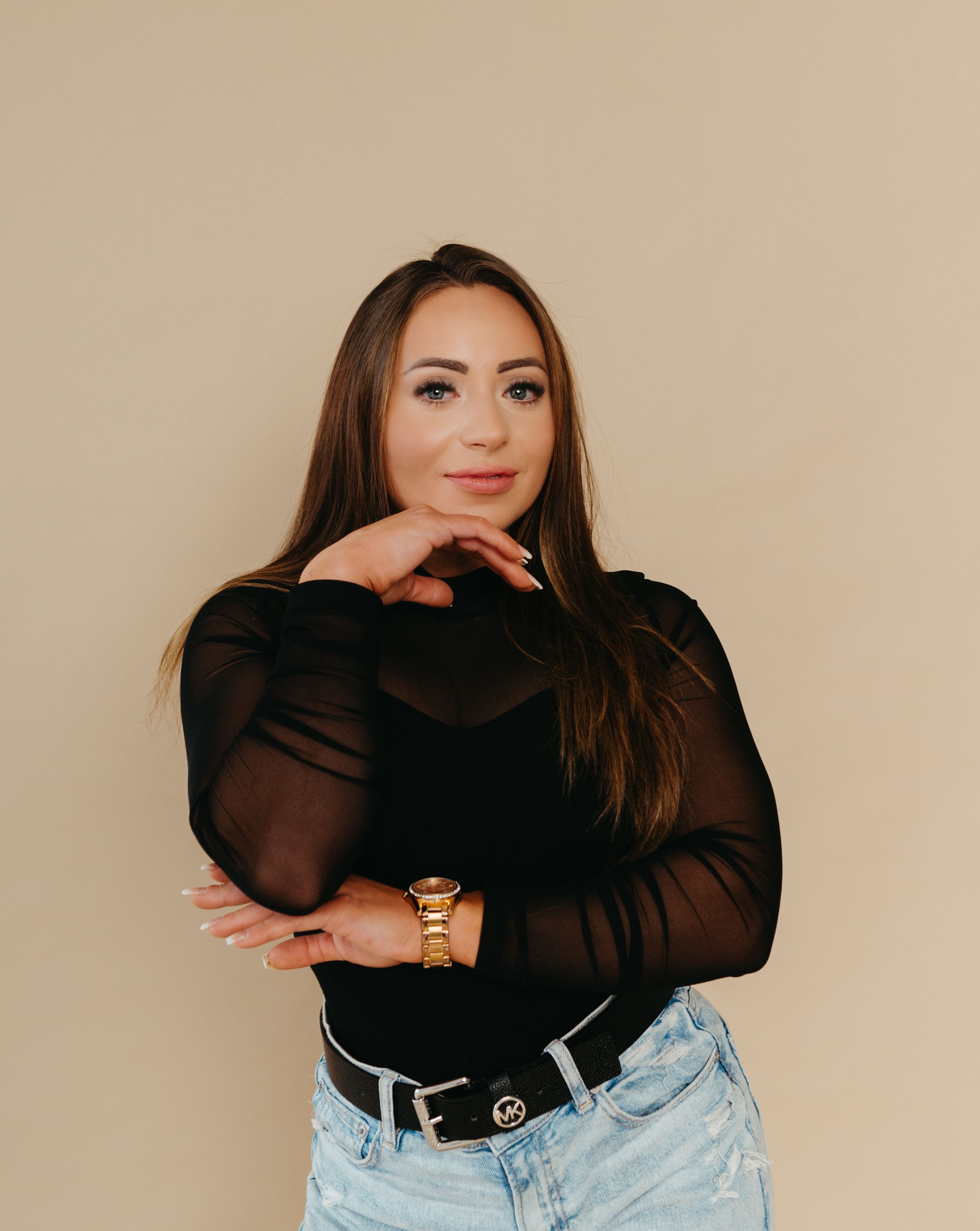 Stylish portrait in sheer black top and light denim against neutral backdrop.
