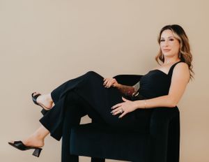 Studio fashion photo featuring all-black ensemble with heels on black furniture.