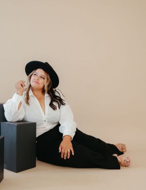 Casual portrait in black hat and white button-down shirt against neutral backdrop.