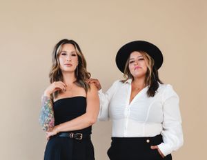 Two people in contrasting black and white outfits pose together against a neutral background.