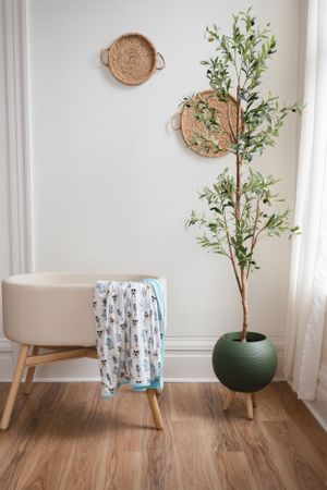 Minimalist interior decor with woven baskets, a beige ottoman, and artificial plant in a green pot.