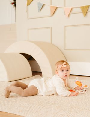 A small child plays near a cream-colored arch tunnel with festive bunting overhead.