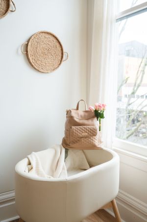 A cozy white modern chair with tan purse and woven wall decor in a bright corner nook.