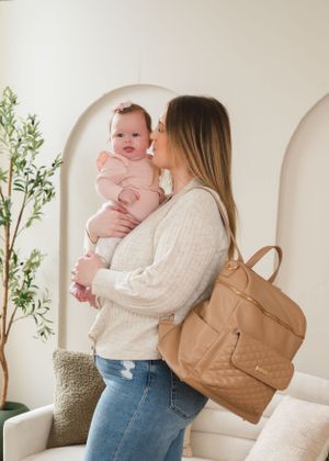 A serene nursery scene with modern furniture, tan diaper bag and natural light streaming through the window.