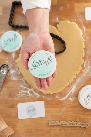 Hand holding a Latirelle cookie stamp over raw cookie dough on wooden surface with baking tools.