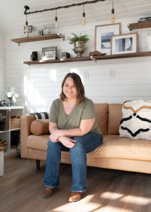 A cozy living room setting with floating wood shelves, a tan leather couch, and decorative lighting fixtures.