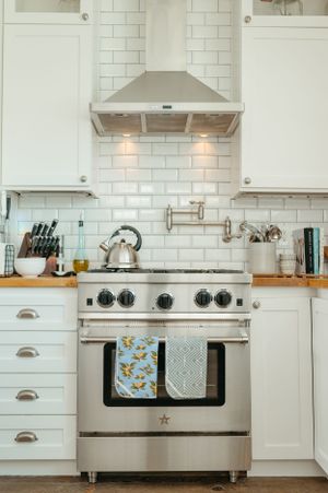 A modern white kitchen with subway tile backsplash and stainless steel range hood.