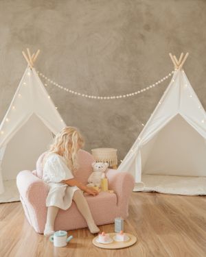 Cozy reading nook with white teepees and pink chair in neutral toned room.