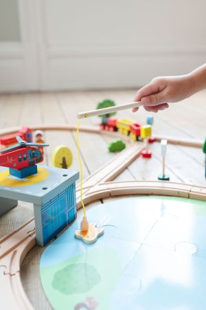 A wooden toy train track setup with colorful accessories and a fishing game component.