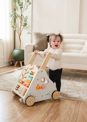 A white push walker toy with colorful decorations on hardwood flooring.