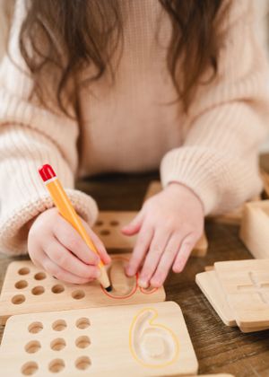 Hands holding a pencil while working with a wooden educational toy board.