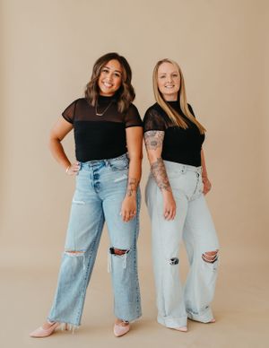 Two people posing in matching black tops and distressed jeans against beige background.