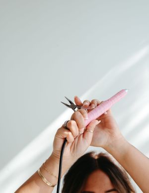 Close-up of hands holding pink scissors against white background with dramatic shadow.